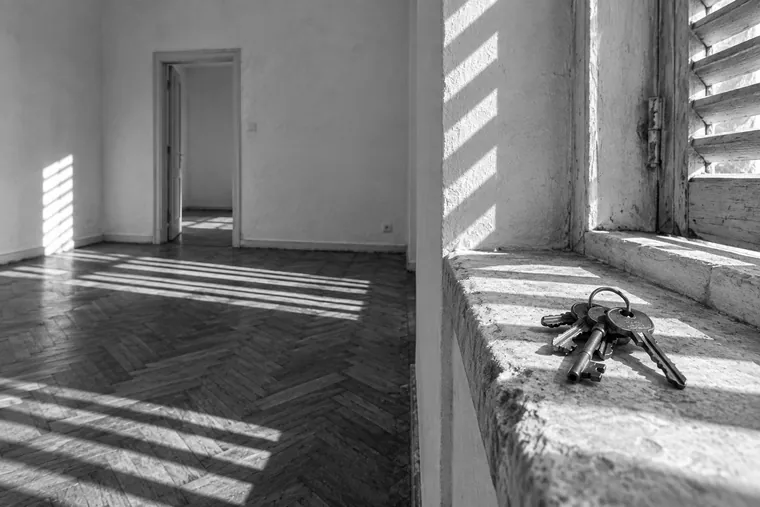 Un trousseau de clés posé sur l’appui de fenêtre d’un appartement vide, les lames d’un volet rayant le sol d’ombres dures